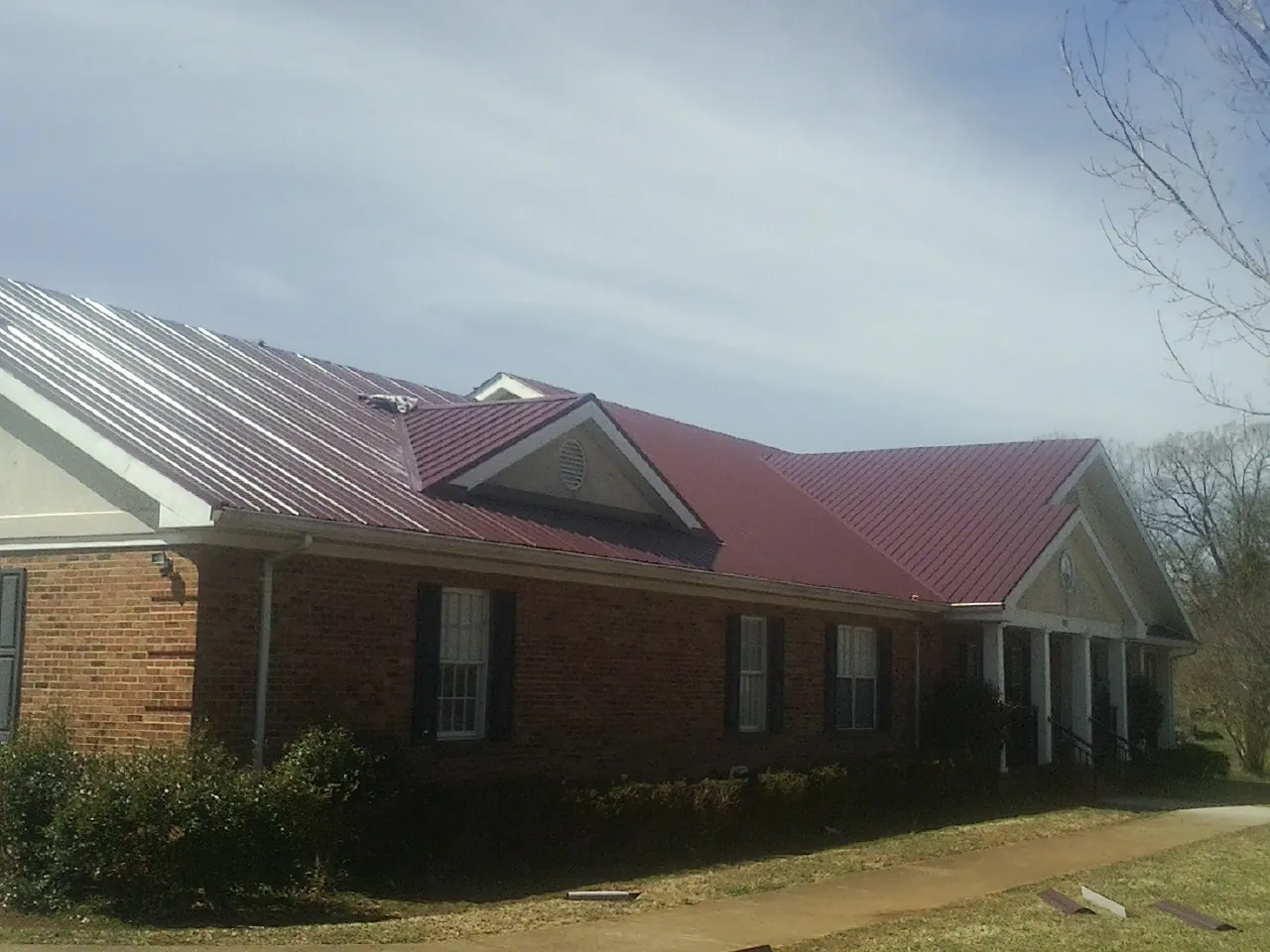 Red metal roof with gabled entries on a long brick building, from a Hail Damage Roof Repair job in Kearney