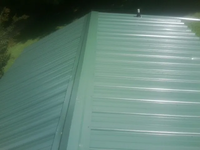 New green metal panels meeting at the ridge of a roof — Flat Roof Repair work by our crew in Kearney