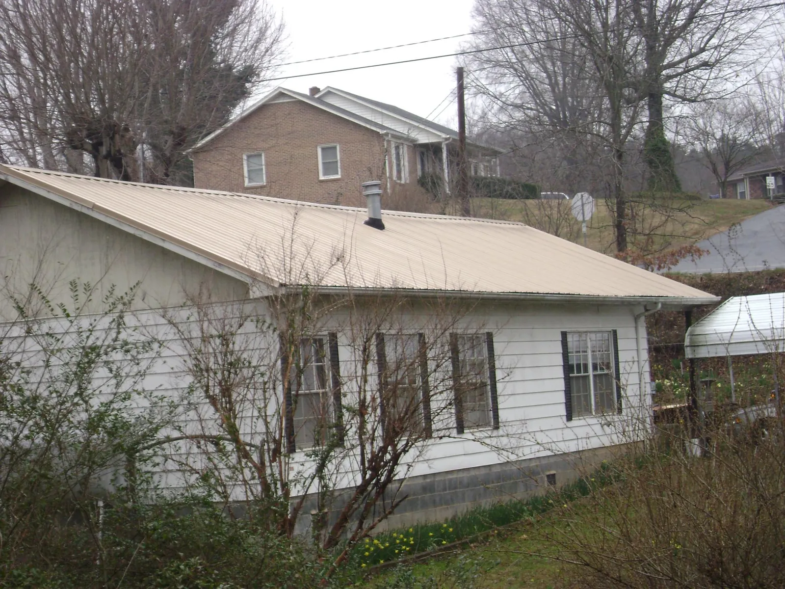Tan metal roof on a white sided house set into a hillside — Commercial Roofing by Roofing Brothers in Kearney